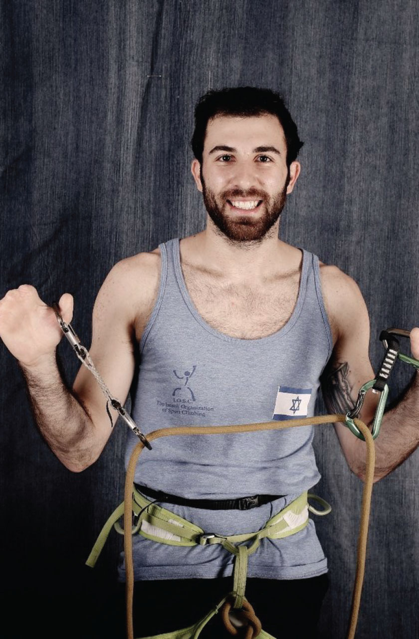 Mor Sapir, wearing his climbing sleeveless shirt holding his climbing tools in both hands on a Dark Grey background